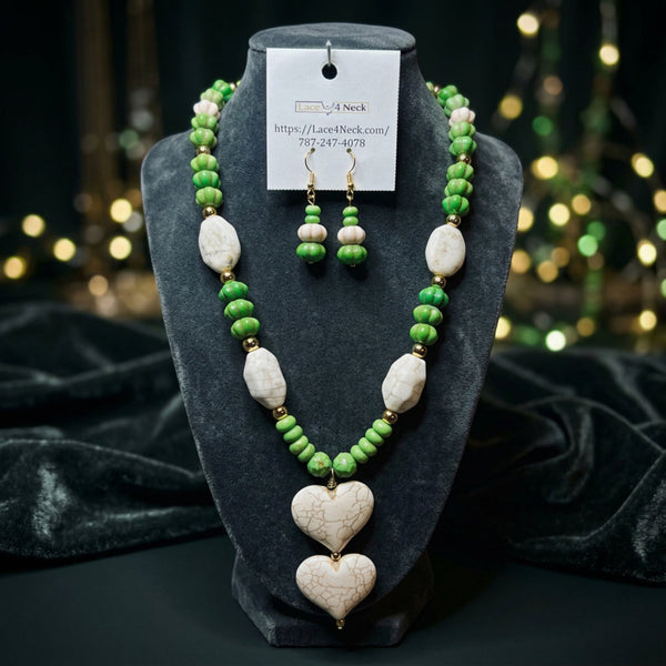 A beaded necklace and matching drop earrings displayed on a cream jewelry bust. The necklace features green beads, white marbled oval beads, and two large white heart-shaped beads with a crackled pattern at the center.