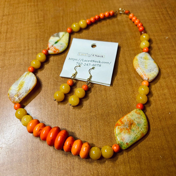 A beaded necklace and matching drop earrings displayed on a wooden surface, with a white card tag reading Lace A Neck. The jewelry features round orange and yellow beads with large marbled stone-like accents in white, orange, and green.