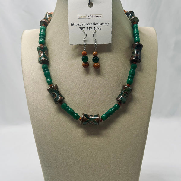 A beaded necklace and matching drop earrings displayed on a beige jewelry bust. The necklace features green beads, dark brown cylindrical beads, and patterned dark beads with metallic details.
