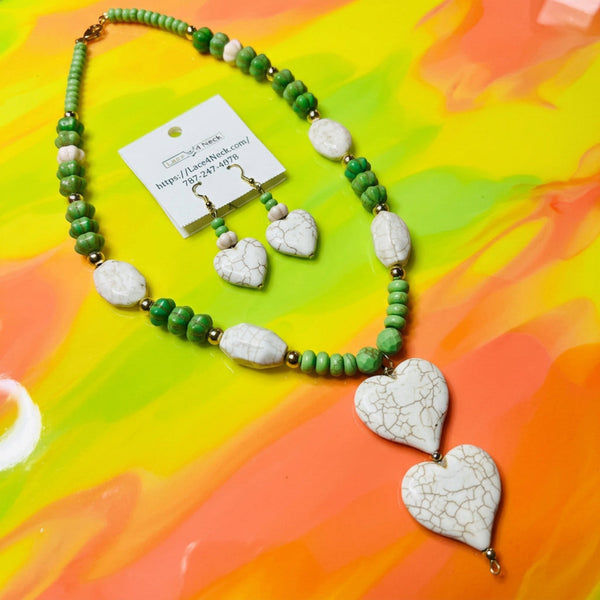 A green and white beaded necklace with matching heart-shaped earrings displayed on a colorful abstract background. The necklace features textured green beads, smooth white beads, and two large white heart charms with a crackled pattern, accompanied by a white display card.