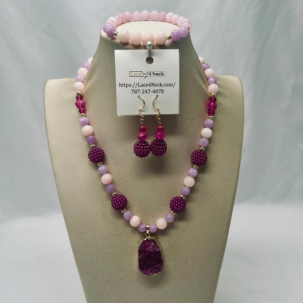 A beaded necklace and matching drop earrings displayed on a beige jewelry bust. The necklace features light pink and lavender beads with faceted purple crystal-like beads and a large purple pendant.