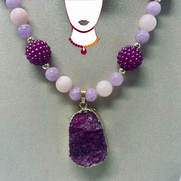 A beaded necklace with lavender and pale pink round beads, two textured dark purple beads, and a large irregular purple geode pendant, displayed on a gray background with a white necklace graphic.