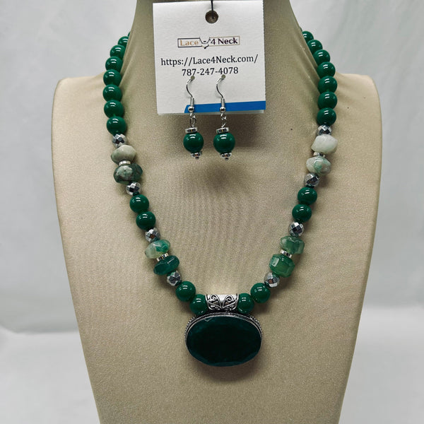 A beaded necklace and matching drop earrings displayed on a beige jewelry bust. The necklace features dark green beads, translucent green stone beads, silver-toned spacer beads, and a large oval dark green stone pendant with silver-toned detailing.