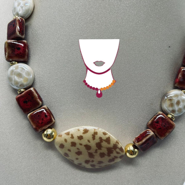 Necklace with maroon, white, and gold beads on a gray background