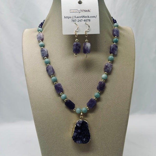 A beaded necklace and matching drop earrings displayed on a beige jewelry bust. The necklace features alternating light blue-green and purple beads with small gold spacer beads, and a large faceted purple geode pendant.