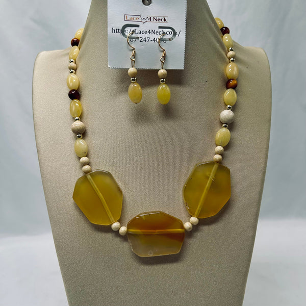 A beaded necklace and matching drop earrings displayed on a beige jewelry bust. The necklace features large translucent yellow agate-like stone shapes with smaller cream and dark brown beads, and the matching earrings have small yellow beads and silver hooks.