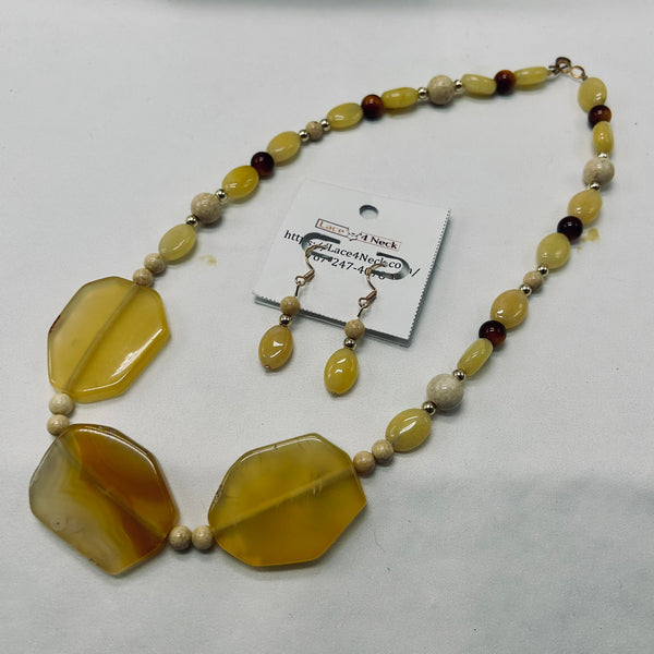 A handmade beaded necklace and matching drop earrings displayed on a white background. The necklace features large, polished yellow-brown agate beads as the focal point, accented with small wooden beads and dark brown beads.