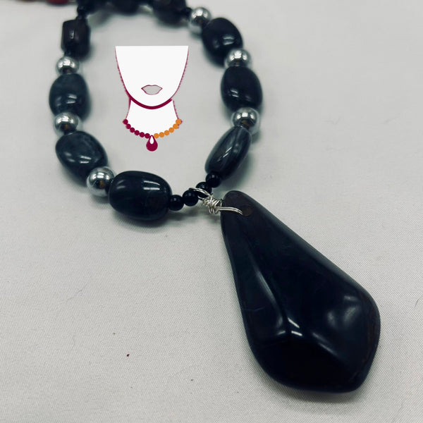 Necklace with black teardrop pendant and silver beads on a light gray background