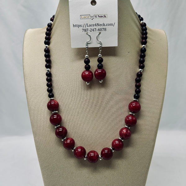 A beaded necklace and matching drop earrings displayed on a beige jewelry bust. The necklace and earrings feature glossy deep red round beads separated by small silver spacer beads, with dark black beads on the upper and lower sections.