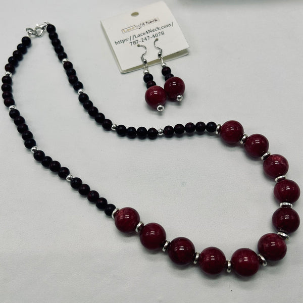 A beaded necklace and matching drop earrings displayed on a white background, with a small product tag attached. The necklace features alternating strands of glossy dark black beads and large polished deep red beads separated by small silver spacer beads.