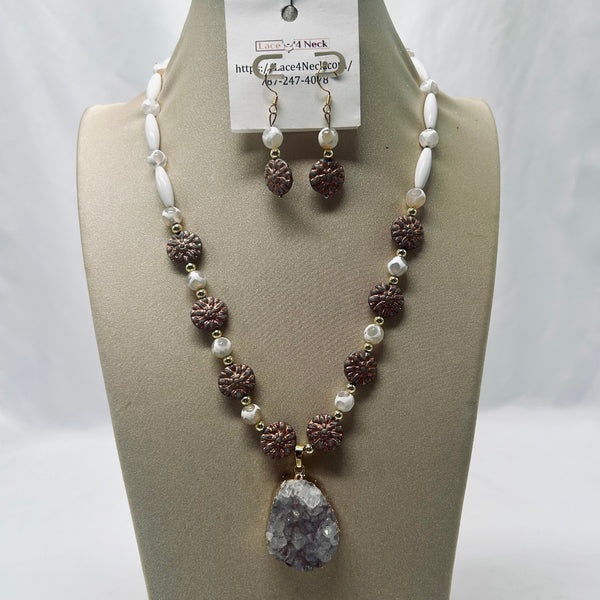 A jewelry set displayed on a beige mannequin bust, featuring a beaded necklace and matching drop earrings. The necklace has white faux pearls, brown textured pine-cone beads, and a large teardrop-shaped gray crystal pendant.