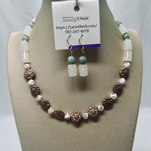 A beaded necklace and matching drop earrings displayed on a beige jewelry bust. The necklace features white faux pearls, light aqua blue beads, and metallic rose-gold textured flower-shaped beads.