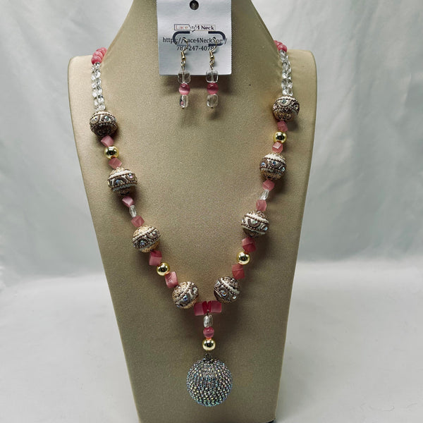 A beaded necklace and matching drop earrings displayed on a beige jewelry bust. The necklace features silver-toned textured beads, pink faceted beads, clear crystal-like beads, and small gold spacer beads, with a large round rhinestone-covered pendant.