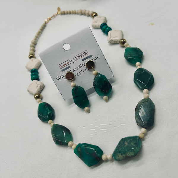 A beaded necklace and matching drop earrings displayed on a white card. The jewelry features faceted dark green stone beads, small white round beads, and polished gold spacer beads.