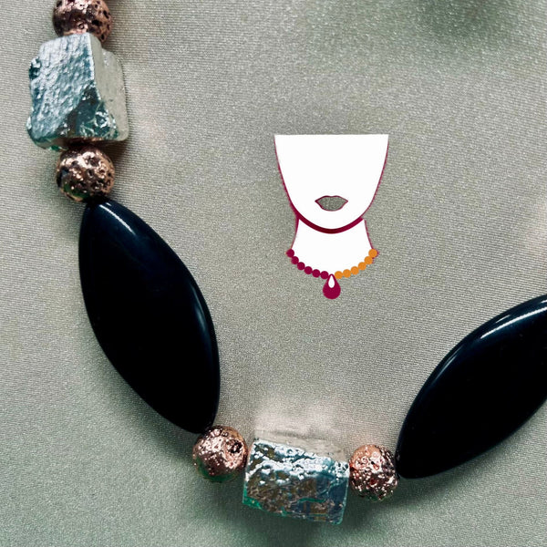 Necklace with large black beads and colorful accents on a textured surface