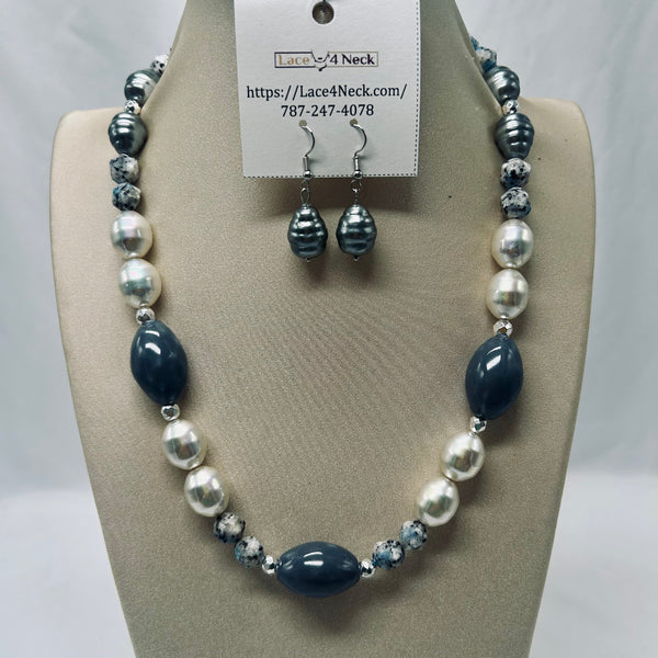 A beaded necklace and matching drop earrings displayed on a beige jewelry bust. The necklace features large glossy navy blue teardrop beads, white pearl-like round beads, and smaller marbled blue-and-white beads separated by silver spacer beads.