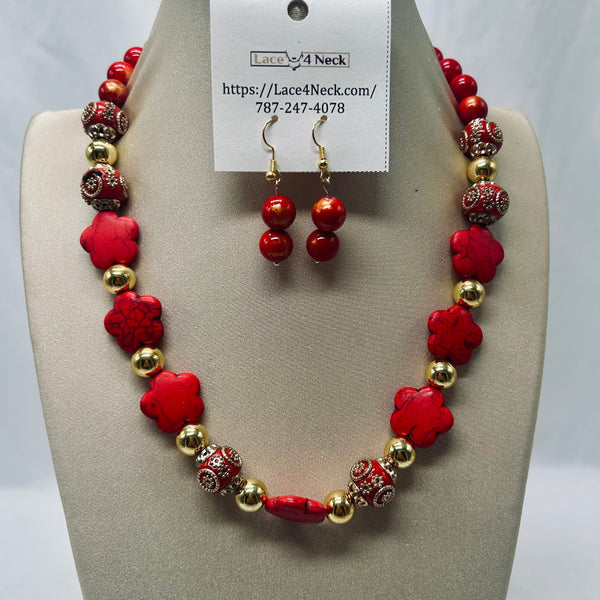 A red and gold beaded necklace with matching drop earrings displayed on a beige jewelry bust. The necklace features red flower-shaped beads, round red beads, and metallic gold-toned spacer beads, with some red beads showing silver rhinestone detailing.