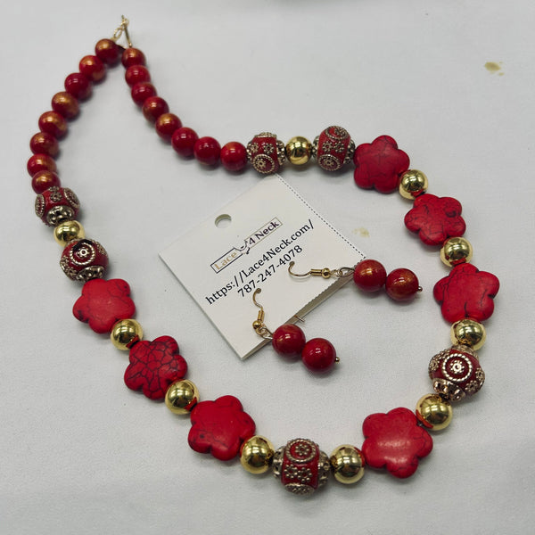 A red and gold beaded jewelry set on a white background, including a necklace, matching earrings, and a product tag. The necklace features red beads, red flower-shaped beads, and textured red and gold spacer beads.