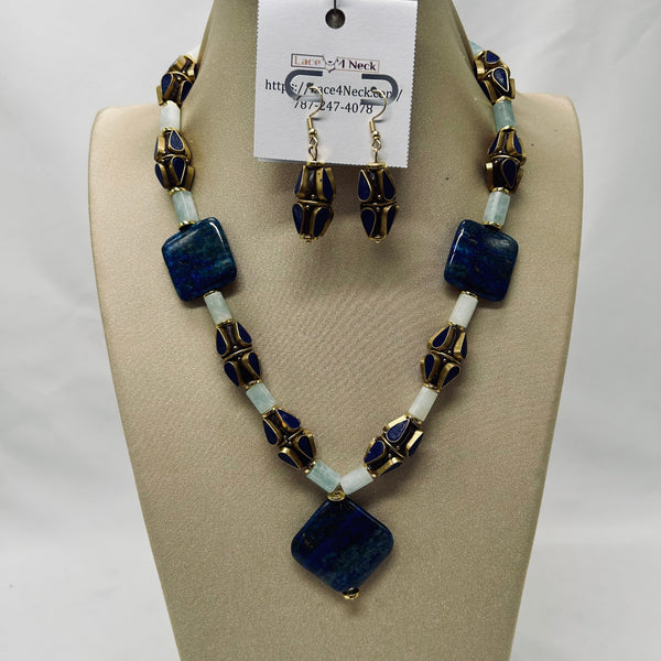 Jewelry set with necklace and earrings on a beige display block, featuring blue and gold beads.