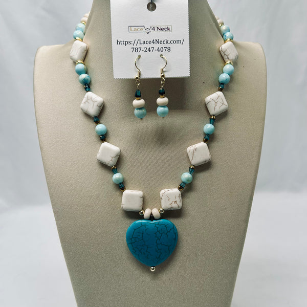 A beaded necklace and matching drop earrings displayed on a beige jewelry bust. The necklace features white marble-like square beads, light blue round beads, and a large turquoise heart pendant.