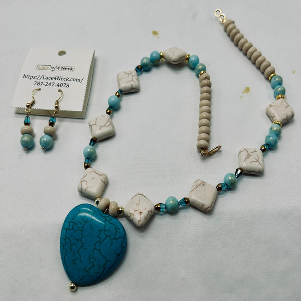 A beaded necklace and matching drop earrings displayed on a white surface. The necklace features light blue beads, cream-colored stone square charms, and a large turquoise heart-shaped pendant.
