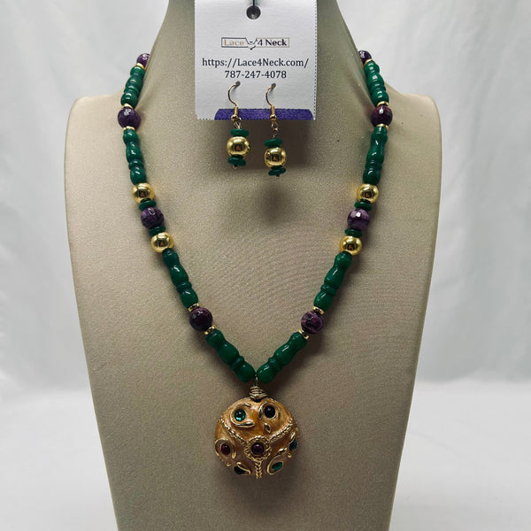 A beaded necklace and matching drop earrings displayed on a beige jewelry bust. The necklace features dark green cylindrical beads, purple faceted beads, and small gold spacer beads, with a gold-toned spherical pendant.