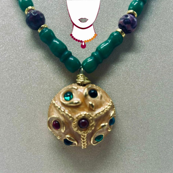 A beaded necklace with dark green cylindrical beads, purple marbled accent beads, and a large ornate gold pendant decorated with green, red, and blue gemstones, displayed on a gray background.