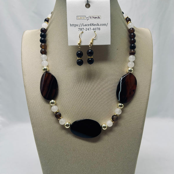 A beaded necklace and matching drop earrings displayed on a beige jewelry bust. The necklace features large dark brown agate oval beads, smaller dark brown and white beads, and small gold-toned spacer beads.