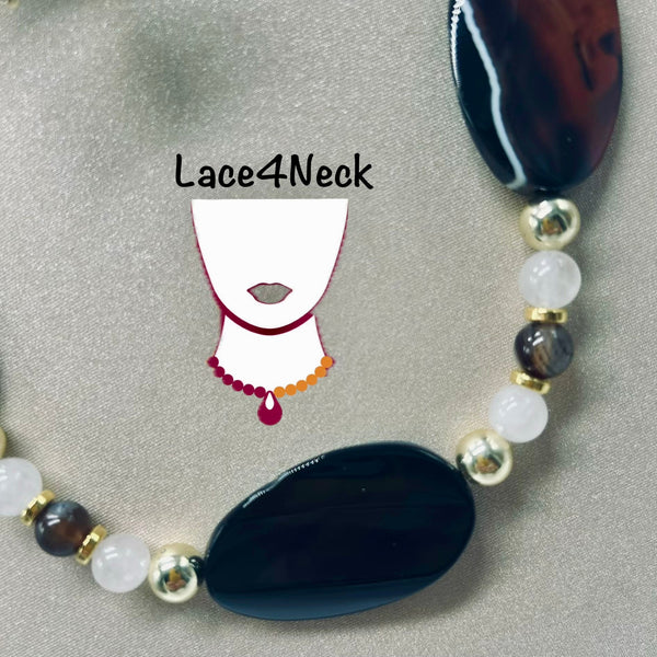 A beaded necklace with large polished dark blue and brown agate-like oval beads, white round beads, and metallic gold spacer beads, displayed on a gray fabric background. A simple necklace graphic with the text 'Lace4Neck' is overlaid in the center.