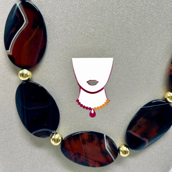 Necklace with dark agate stones and gold beads on a gray background