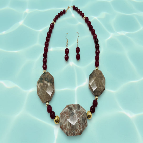 Necklace and earrings set with maroon beads and stone-like pendants on a white background.