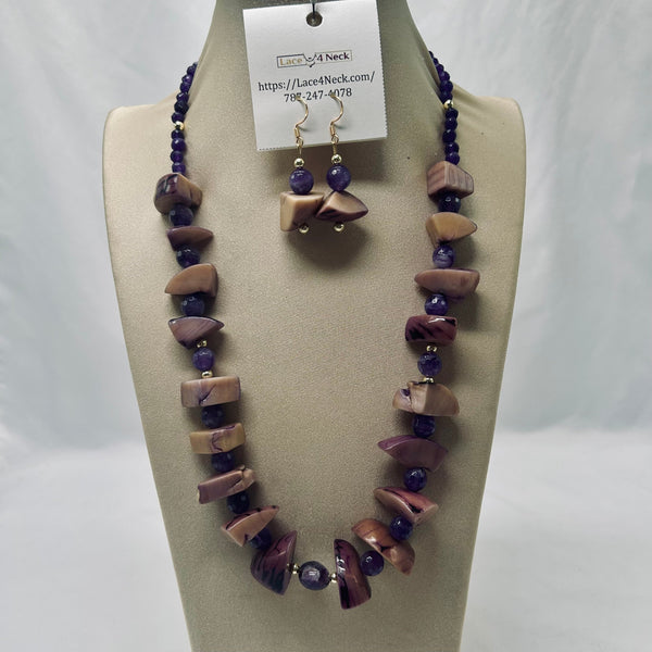 A necklace and matching drop earrings displayed on a beige jewelry bust. The jewelry features irregular polished stone beads in mauve, lavender, and taupe tones, accented with small dark purple faceted beads and silver-toned spacers.