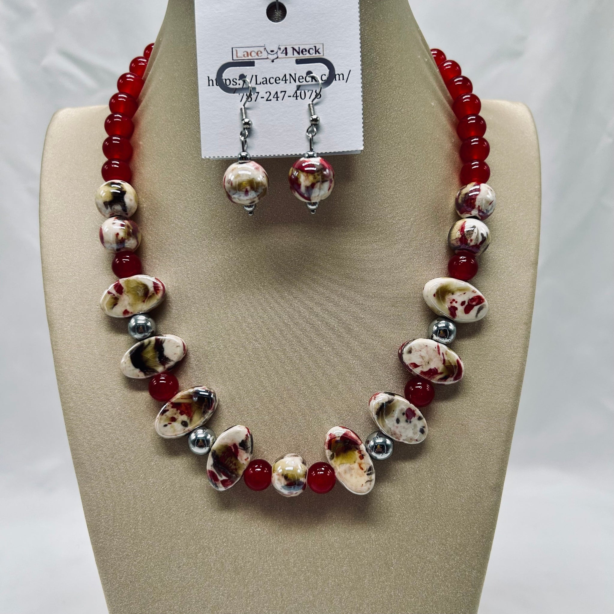 Jewelry set with red and white beads on a beige display block, featuring a necklace and earrings.
