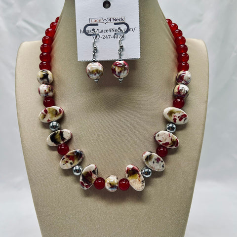 Jewelry set with red and white beads on a beige display block, featuring a necklace and earrings.