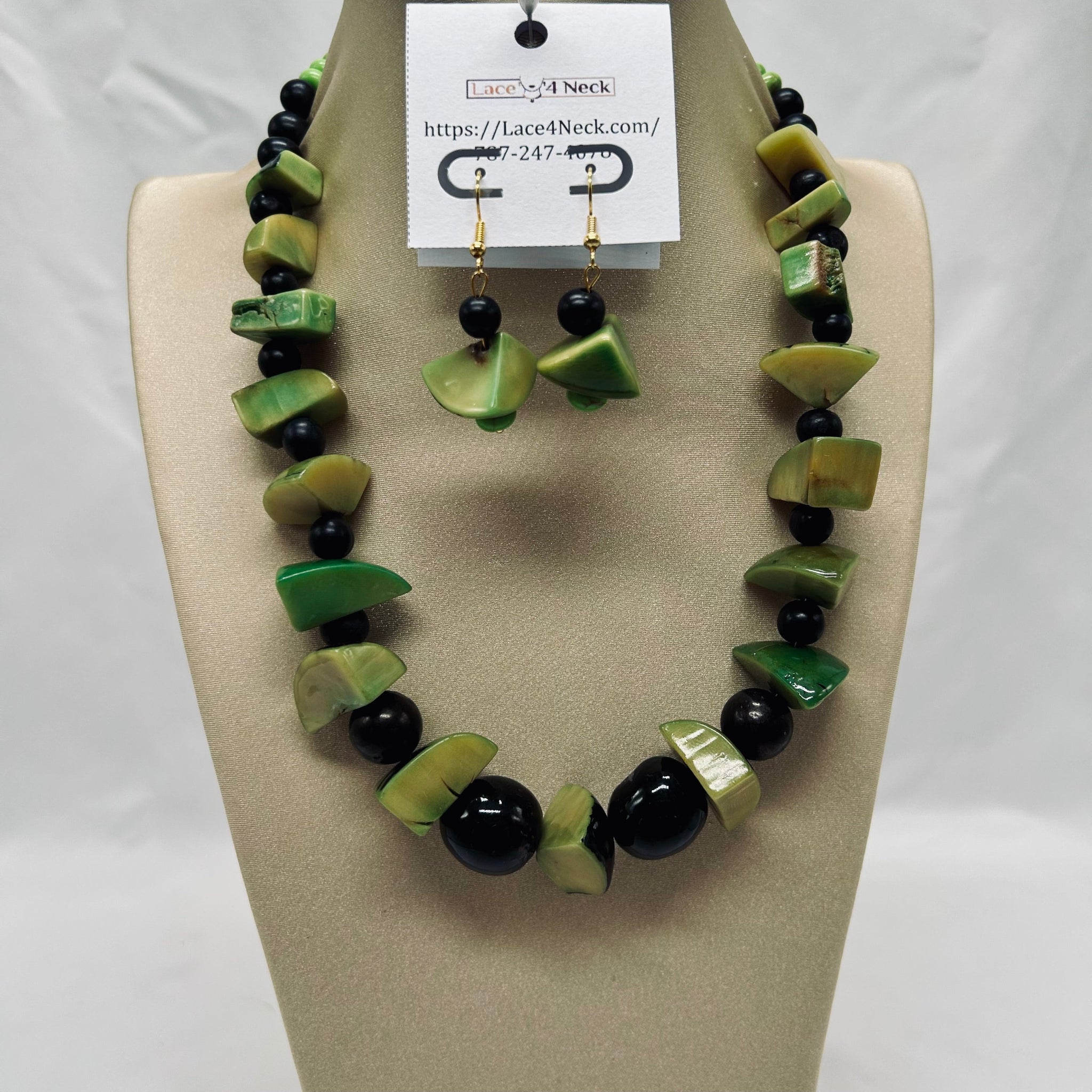 Necklace and earrings set with green and black beads on a beige display stand.