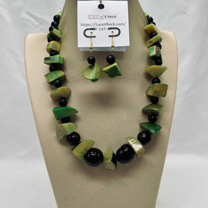 Necklace and earrings set with green and black beads on a beige display stand.