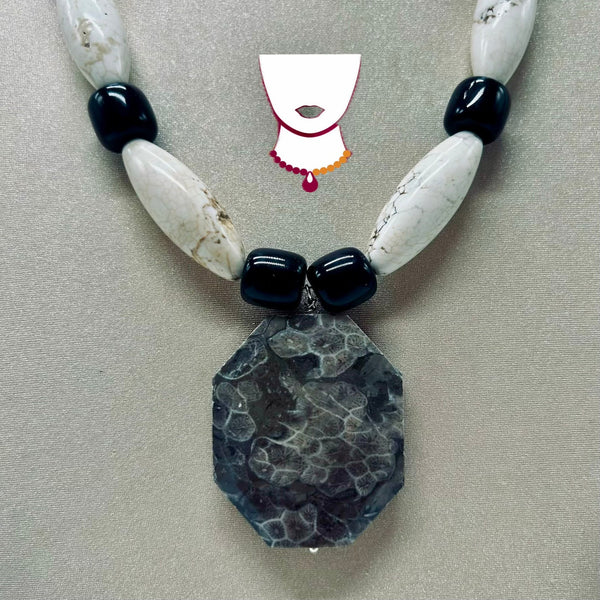 Necklace with large stone pendant and black and white beads on a neutral background