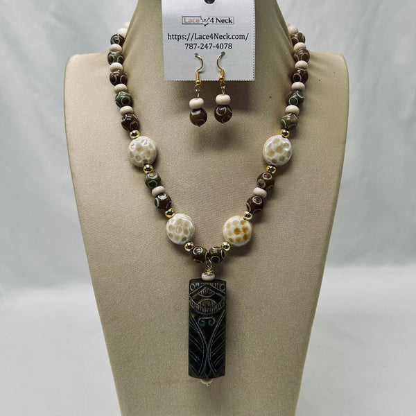 A beaded necklace and matching drop earrings displayed on a beige jewelry bust. The necklace features dark brown and cream beads with a carved black pendant, and the matching earrings are shown above the necklace on a white card labeled Lace4Neck.