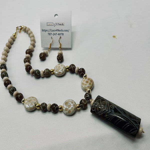 A beaded necklace and matching drop earrings displayed on a white background with a product tag. The necklace features a mix of dark brown, beige, and white marbled beads with small gold spacer beads and a large carved black cylindrical pendant.