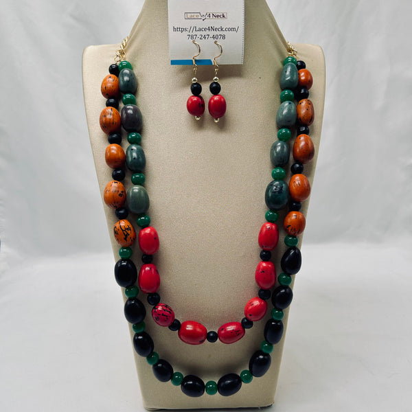 A beaded necklace and matching drop earrings displayed on a cream jewelry bust. The necklace features large polished red beads, dark green beads, and smaller orange and black beads, with gold-tone hooks.