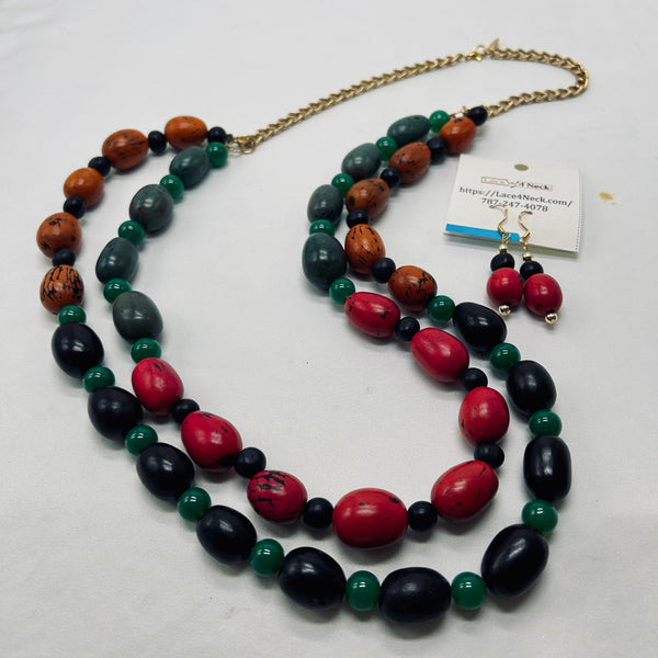 A beaded necklace and matching drop earrings displayed on a white surface. The necklace features large oval beads in red, black, and green, with a gold-tone chain.