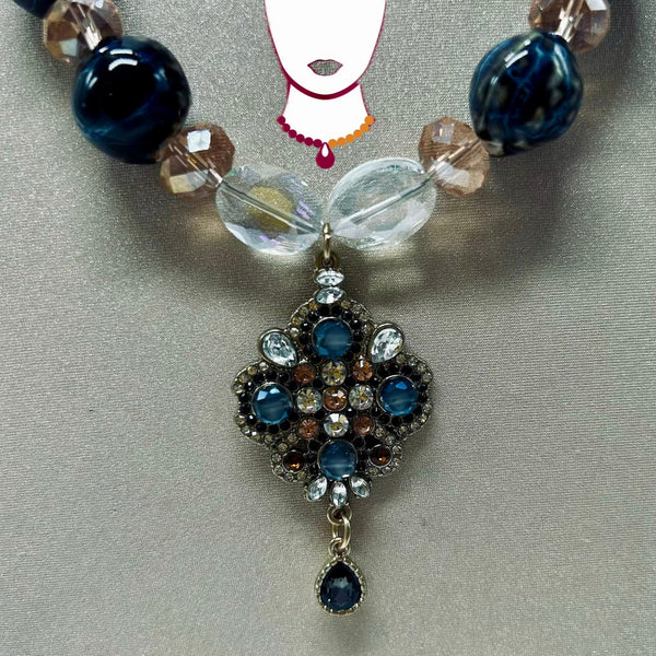 Necklace with blue and clear beads and a decorative pendant on a gray background