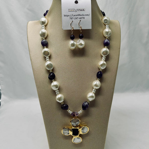 A beaded necklace and matching drop earrings displayed on a beige jewelry bust. The necklace features irregular white pearls, dark purple beads, small silver spacer beads, and a gold-tone cross pendant with clear rhinestones and a black center.