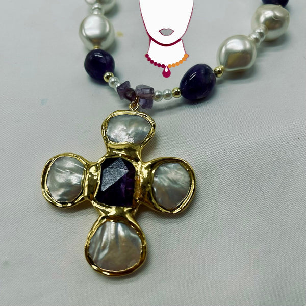 A close-up of a beaded necklace with a gold cross pendant. The necklace features white freshwater pearls, dark purple amethyst beads, and small faceted purple and silver beads.