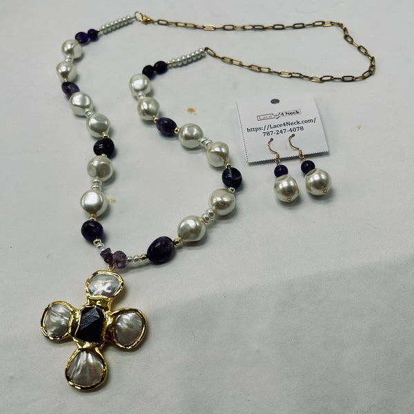 A beaded necklace and matching drop earrings displayed on a light gray surface. The necklace features white freshwater pearls, dark purple amethyst beads, and gold-toned chain and settings, with a cross-shaped pendant made of white pearls and a central dark purple stone.