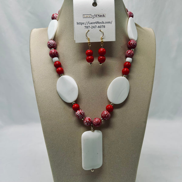 A red and white beaded necklace with a large white rectangular pendant is displayed on a beige jewelry bust, with matching red-and-white beaded drop earrings hanging from a branded paper tag at the top.
