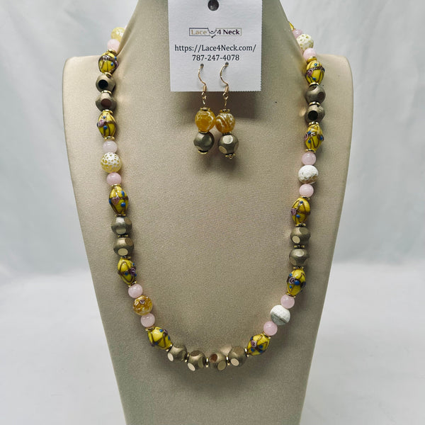 A beaded necklace and matching drop earrings displayed on a beige jewelry bust against a white backdrop. The necklace features marbled yellow and black beads, gray and white beads, and pale pink beads, with a white tag attached at the top.