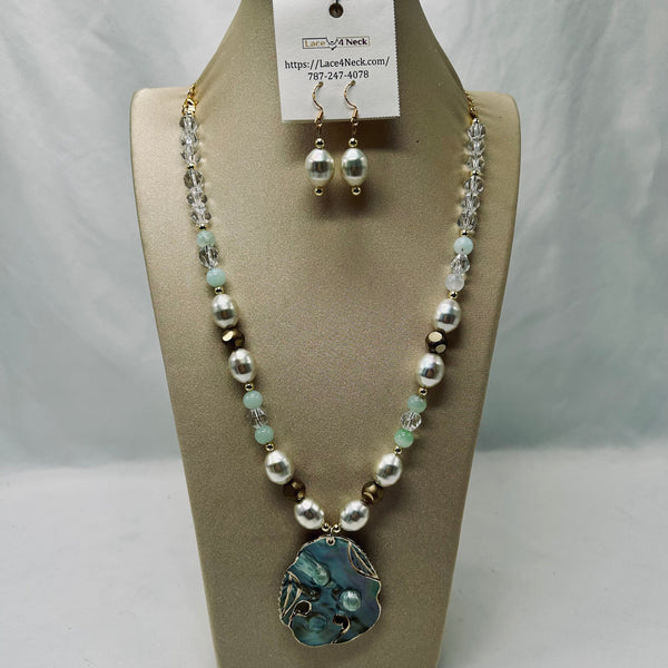 A beaded necklace and matching drop earrings displayed on a beige jewelry bust. The necklace features white freshwater pearls, light green beads, clear faceted crystal beads, and a large irregular blue-green stone pendant with gold-toned metal findings.