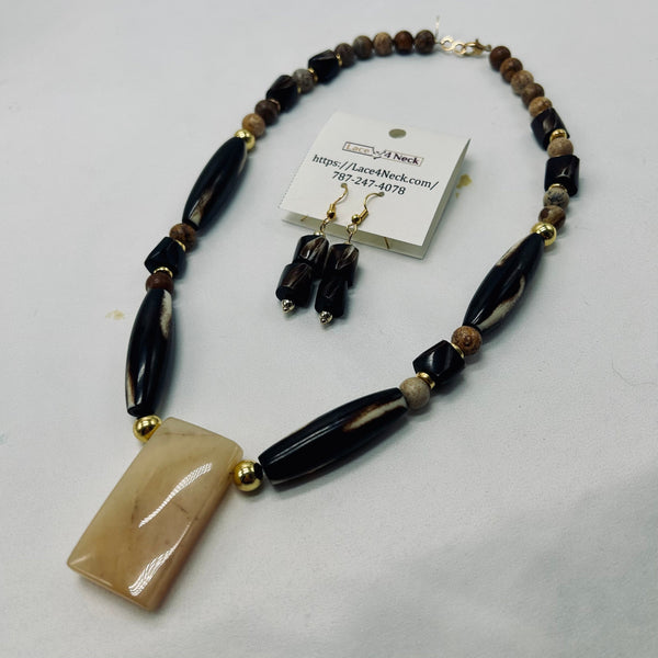 A beaded necklace and matching drop earrings displayed on a white surface. The necklace features large glossy black beads, smaller brown and beige accent beads, gold-tone spacer beads, and a rectangular beige stone pendant.
