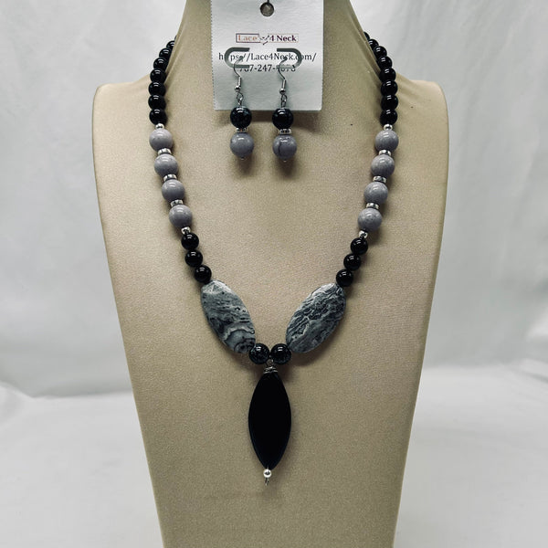 A beaded necklace and matching drop earrings displayed on a beige jewelry bust. The necklace features black round beads, gray marbled oval beads, and a large black teardrop pendant.